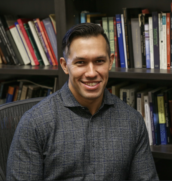 Dr. Charles Stocking, scholar of ancient sport, seated in front of a bookshelf